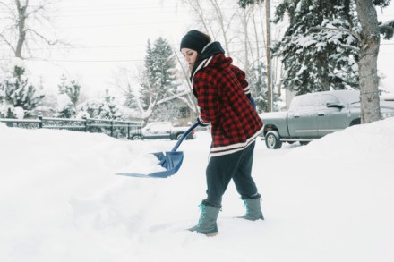 woman-shoveling-snow-on-pine-trees-background_23-2147803895