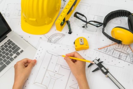 hand-over-construction-plans-with-yellow-helmet-and-drawing-tool_1232-2909